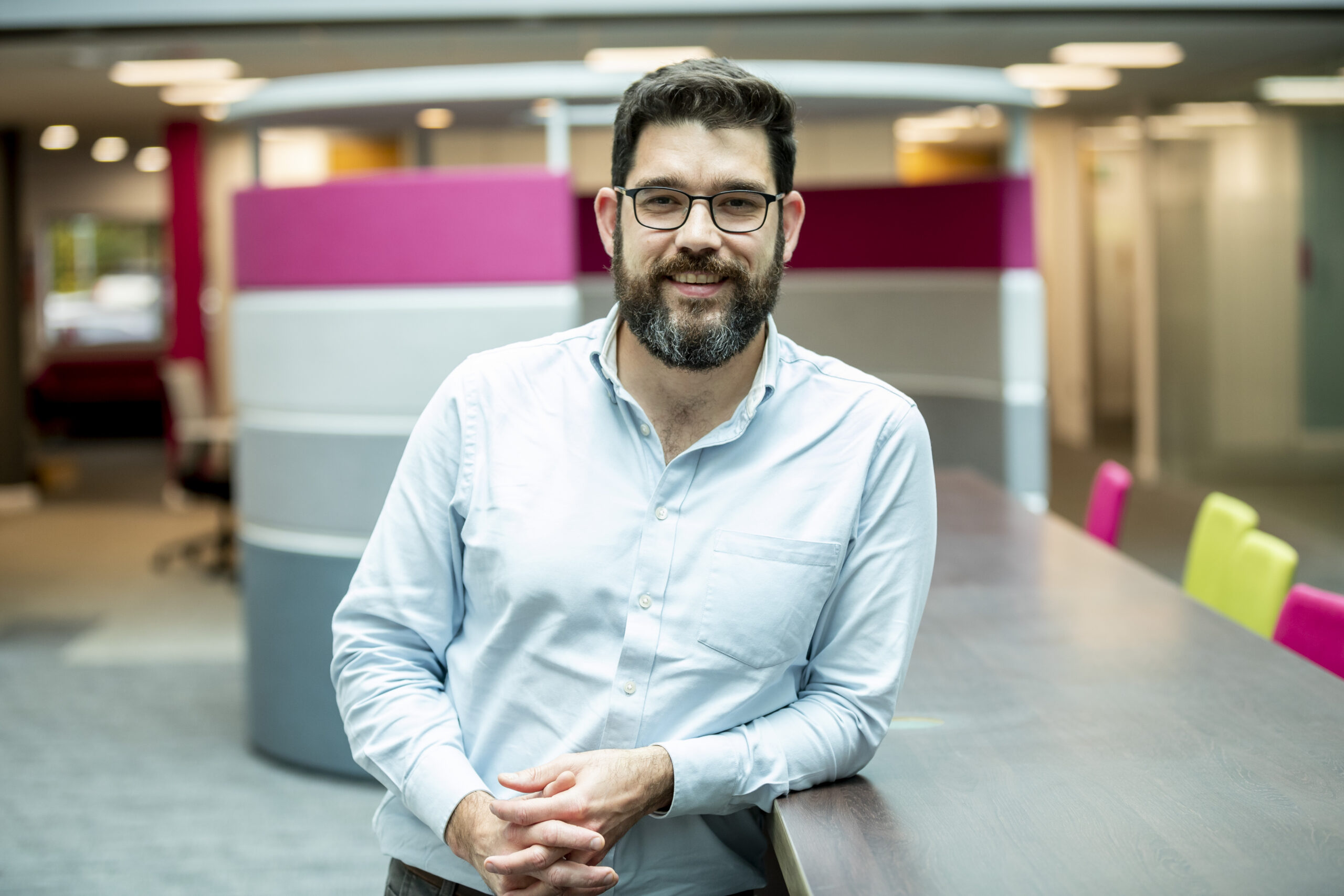 A picture of Emyr George, Director of Qualifications Policy and Reform at Qualifications Wales, wearing a white shirt, leaning in a relaxed way against a desk