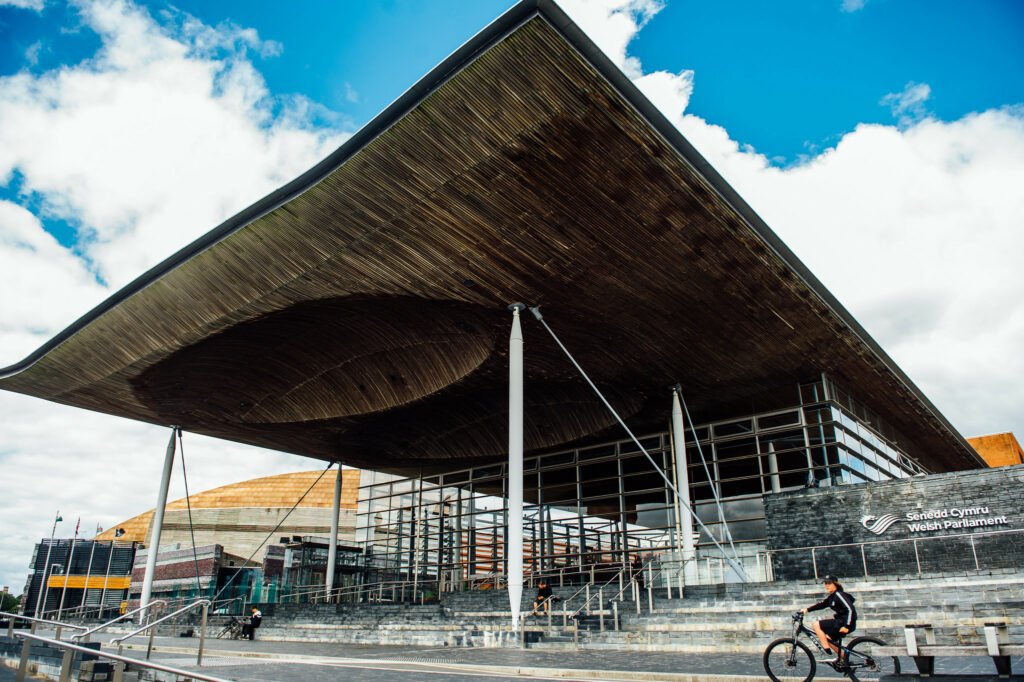 Sir Paul Silk reflects on the history of devolution, 25 years on from the Wales Government Act. The picture shows the Senedd on a sunny day with a blue sky and some clouds in the background.