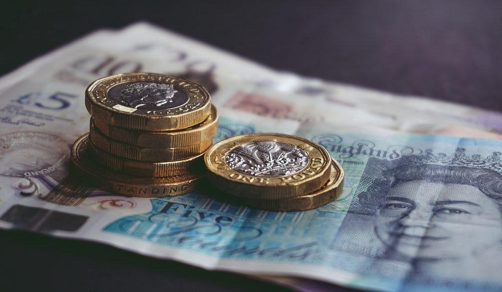 A five pound bill covered with coins. Dr John Ball argues that the Welsh Government's proposed Universal Basic Income (UBI) falls at the first hurdle without major changes.