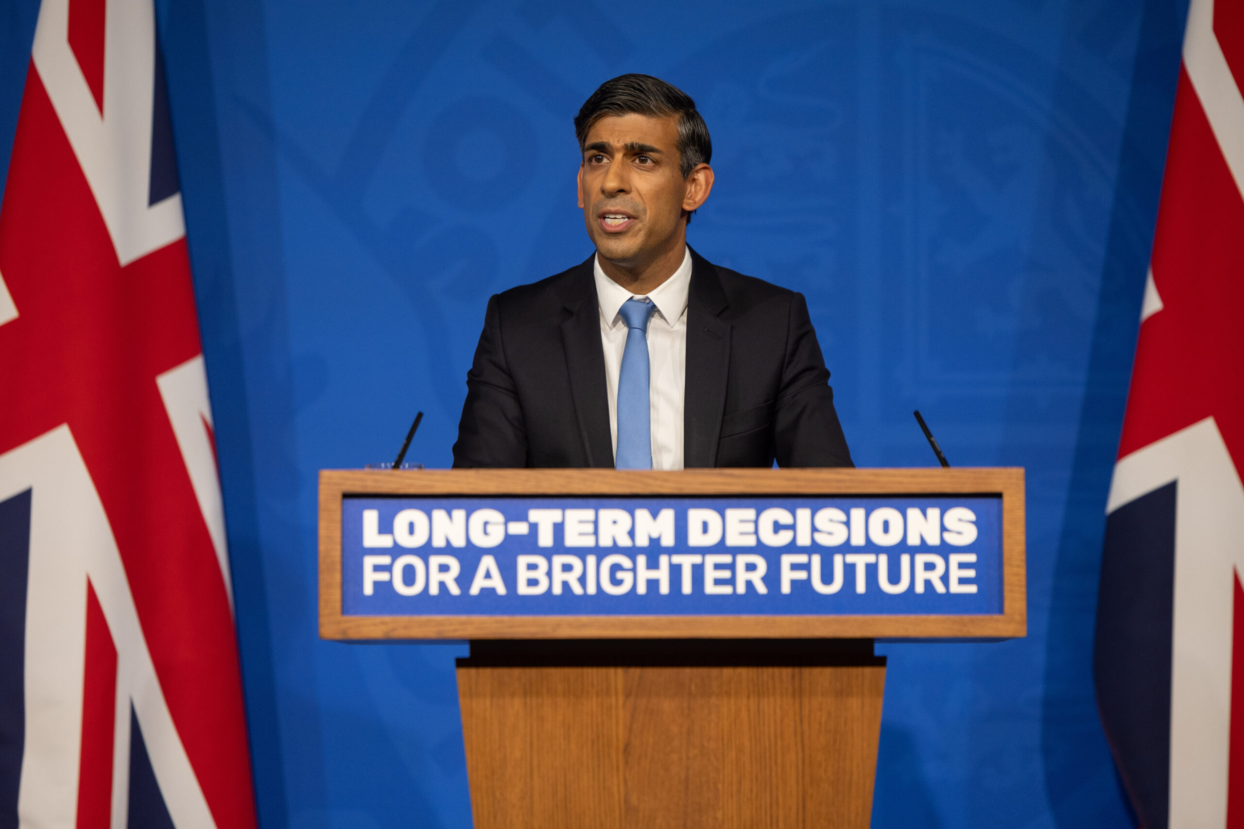 Rishi Sunak holding a Net Zero press conference. He is standing at a lectern stating 'Long-term decisions for a brighter future' in front of a blue background.