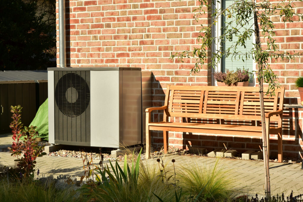 Heat pump next to a wall and a bench.