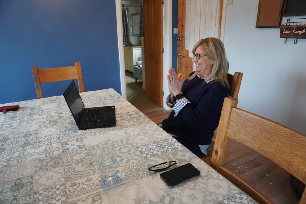 A picture of Donna Jenkins, a participant the Welsh National Opera's programme to help people with Long-Covid. Donna, a blonde woman with glasses and a navy jumper, is attending one of the programmes' sessions on Zoom.
