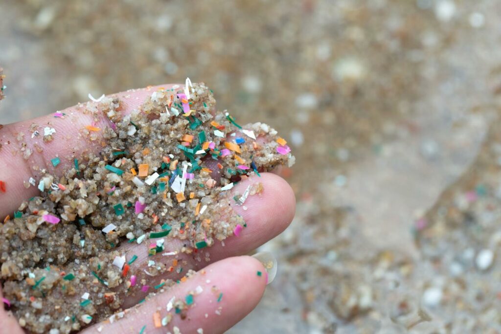 A picture showing a handful of sand, containing small bits of plastic. The article examines the harmful effects of microplastics.